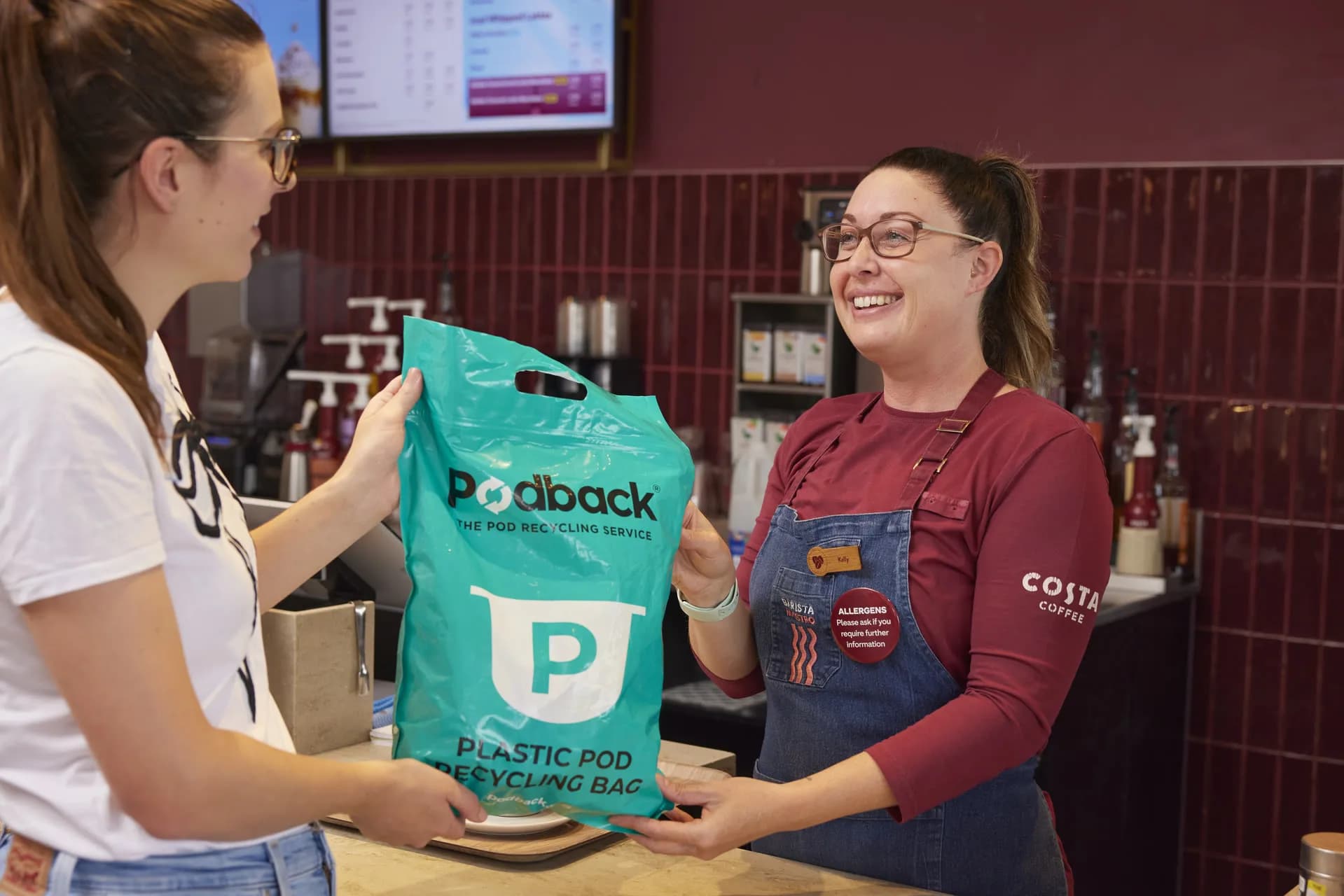 A Costa barista handing a customer a Podback plastic pod recycling bag over the counter