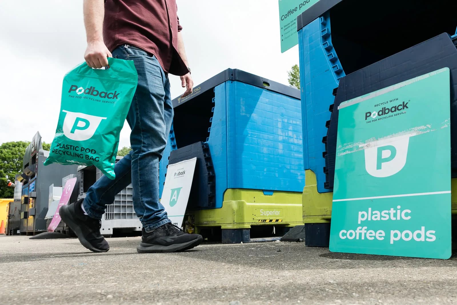 A customer carrying a Podback plastic pod recycling bag to the coffee pod bins at a recycling centre