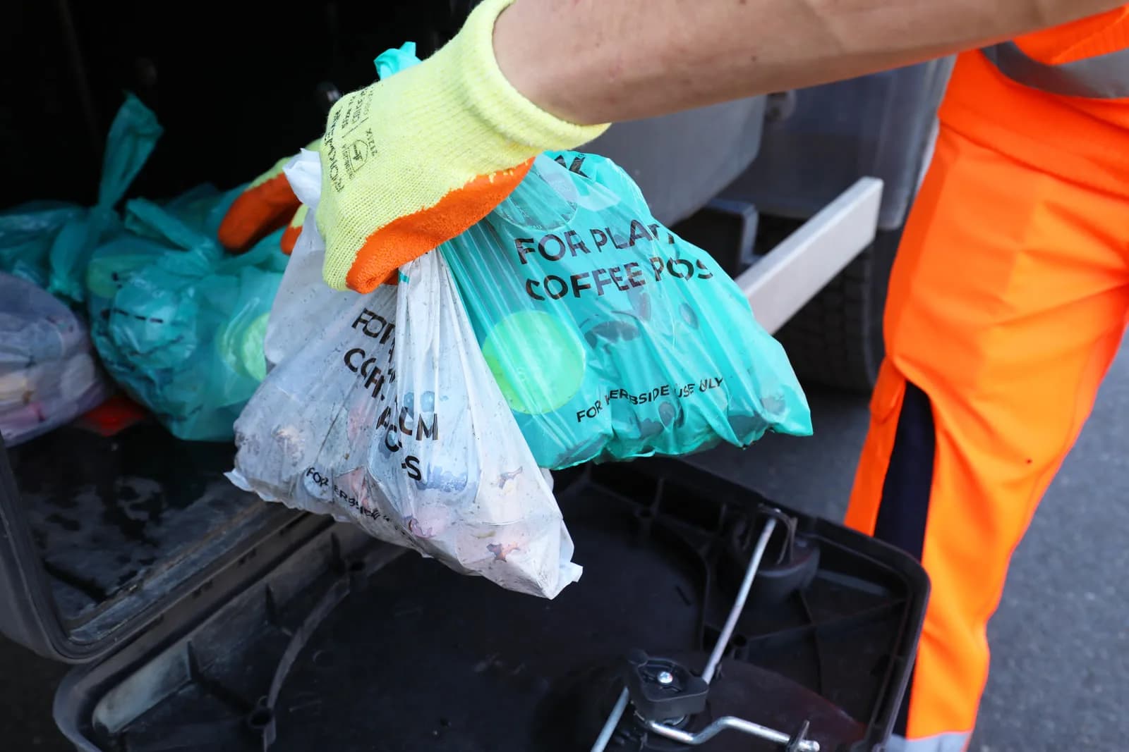A refuse collector holding Podback kerbside bags of used coffee pods at the collection vehicle